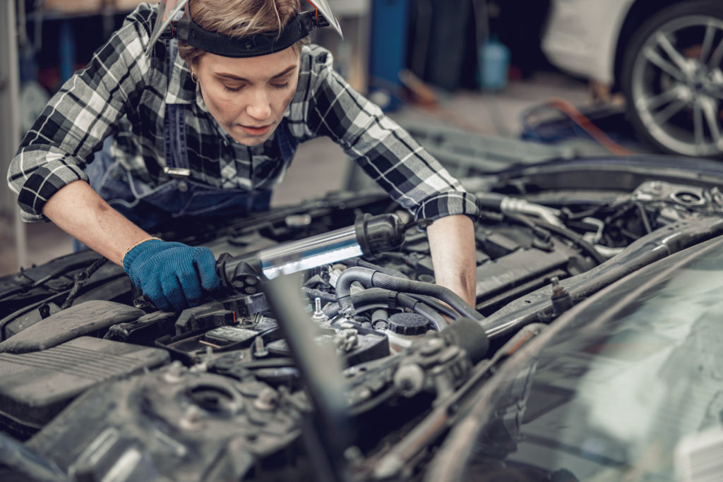 professional car mechanic looking under the hood of a vehicle in an auto repair shop