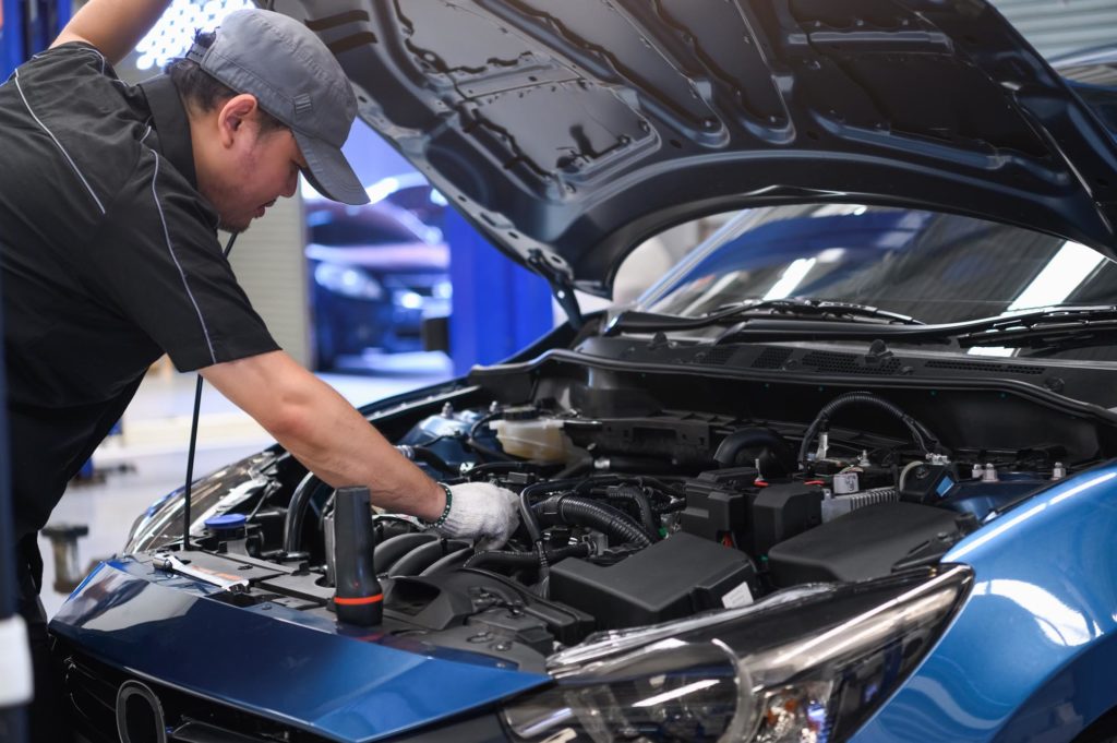 Asian auto mechanic examines car engine