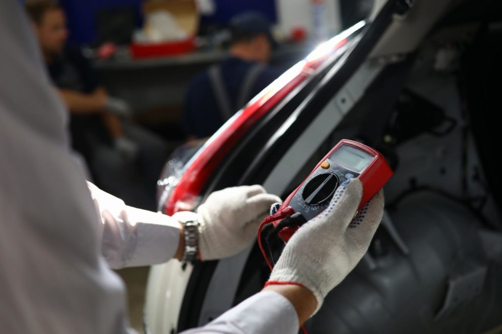 auto mechanic using red voltmeter in focus