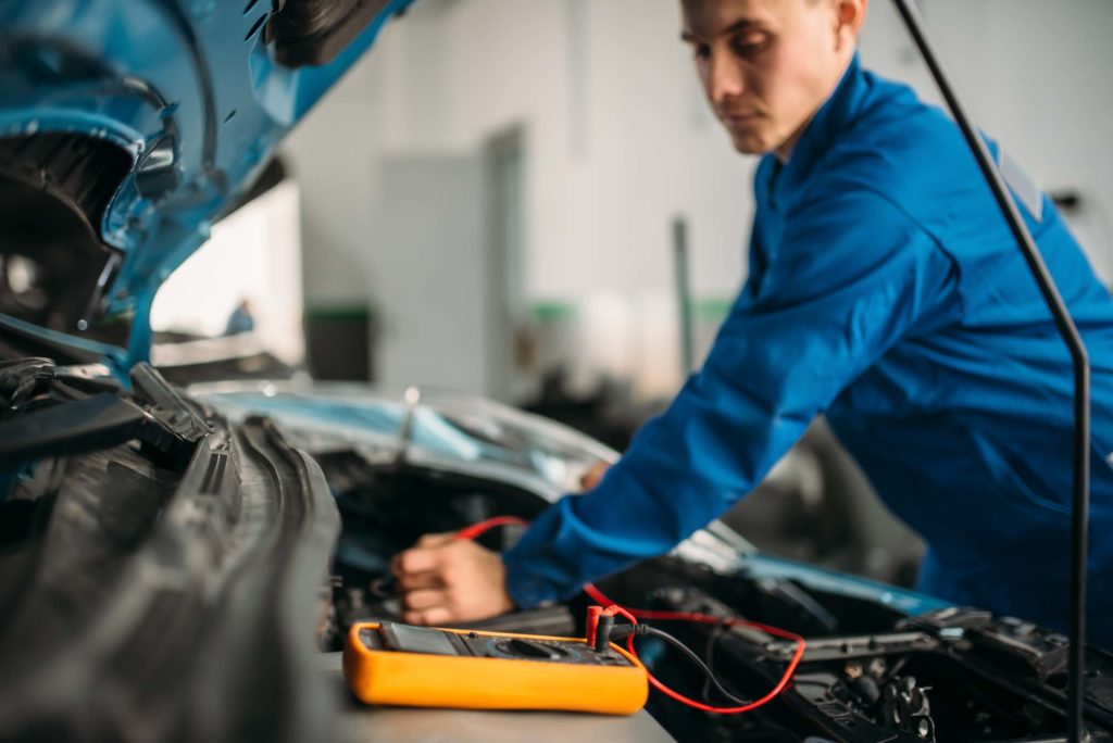 mechanic using a multimeter to perform tests on automotive battery