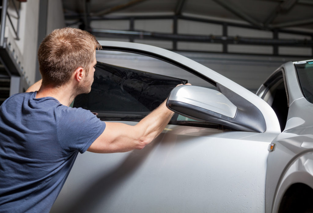 male in garage applying tint film on car window