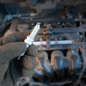 hand holding a spark plug beside a car engine