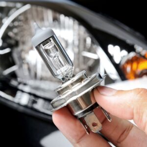 hand holding a halogen bulb in front of a car headlight