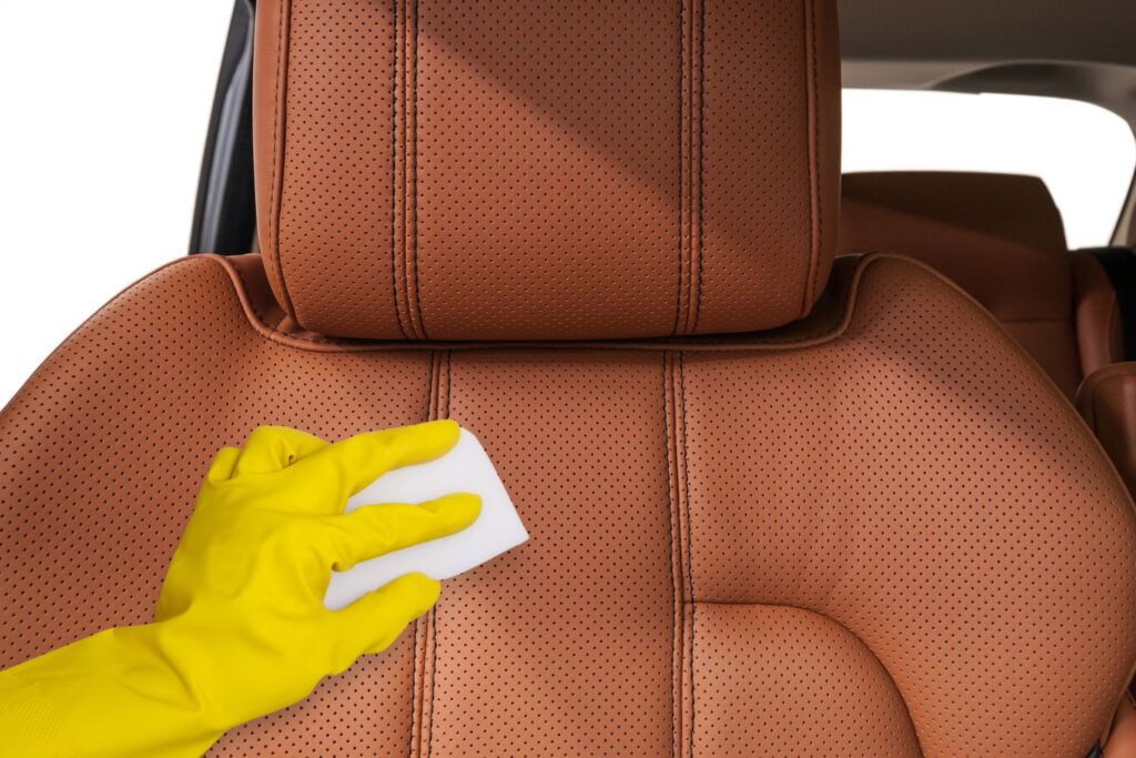 hand wearing glove holding a magic eraser on a car leather seat
