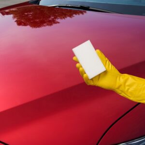 hand holding a magic eraser beside a car hood