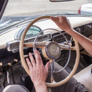 person holding the steering wheel of a classic car