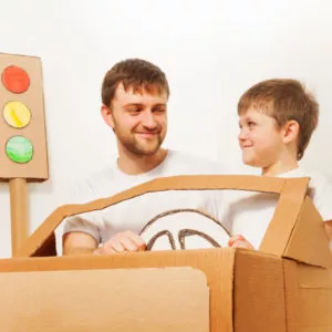 father son driving cardboard car at home scaled e1586832654122