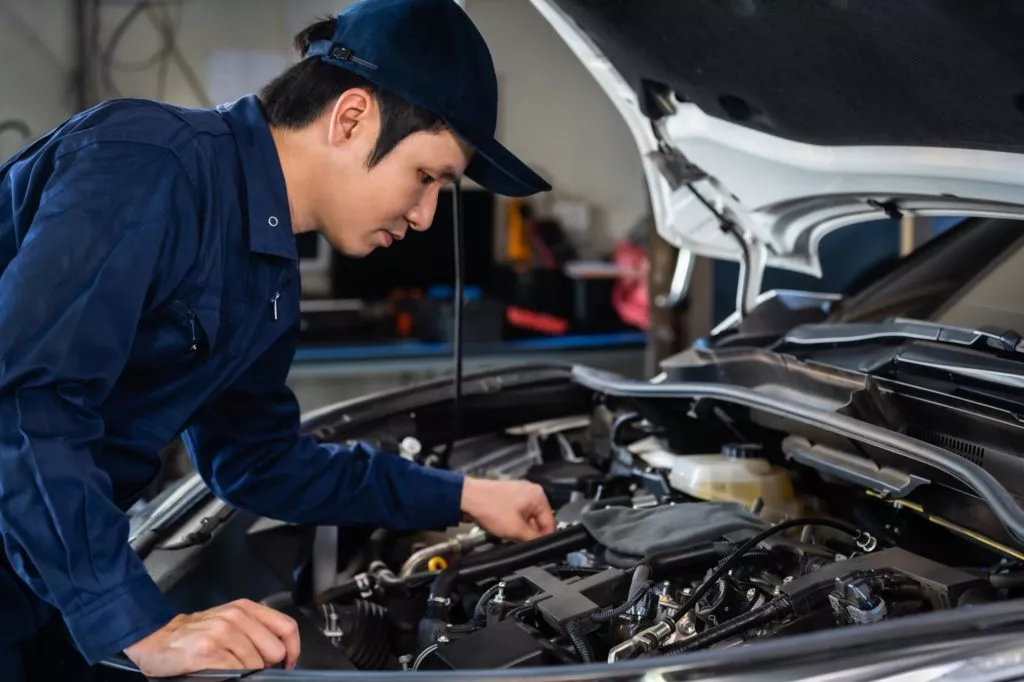 asian mechanic checking under the car hood