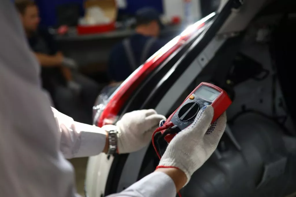 auto mechanic using red voltmeter in focus