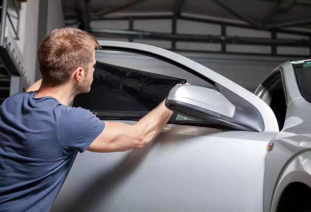 male in garage applying tint film on car window
