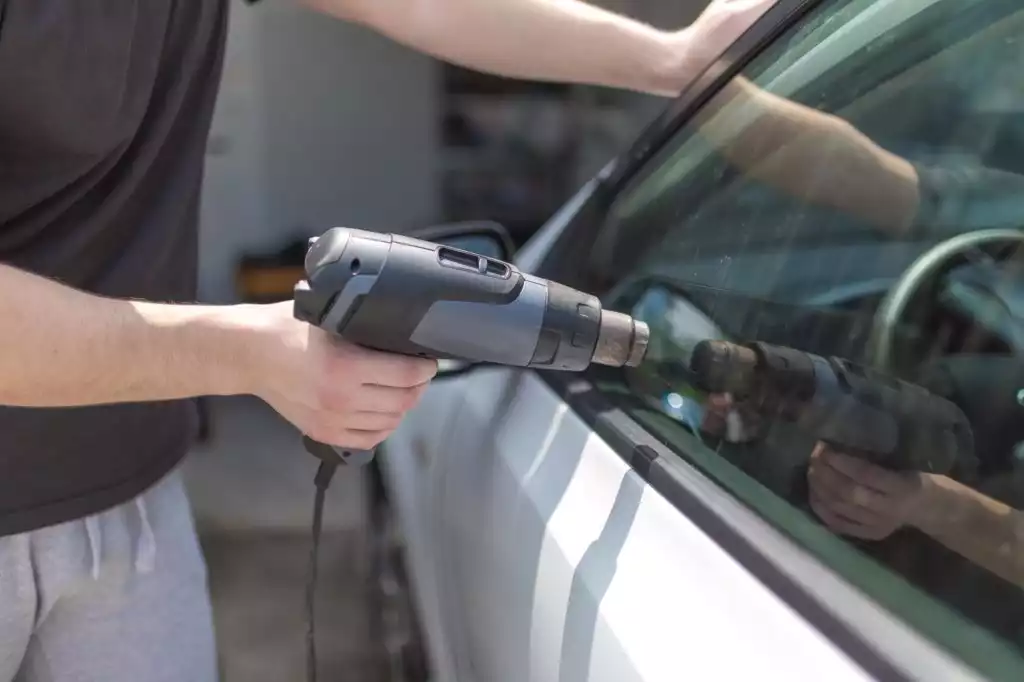 man using heat gun to remove car tint film