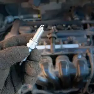 hand holding a spark plug beside a car engine