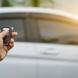 hand holding a key fob with a white car at the back