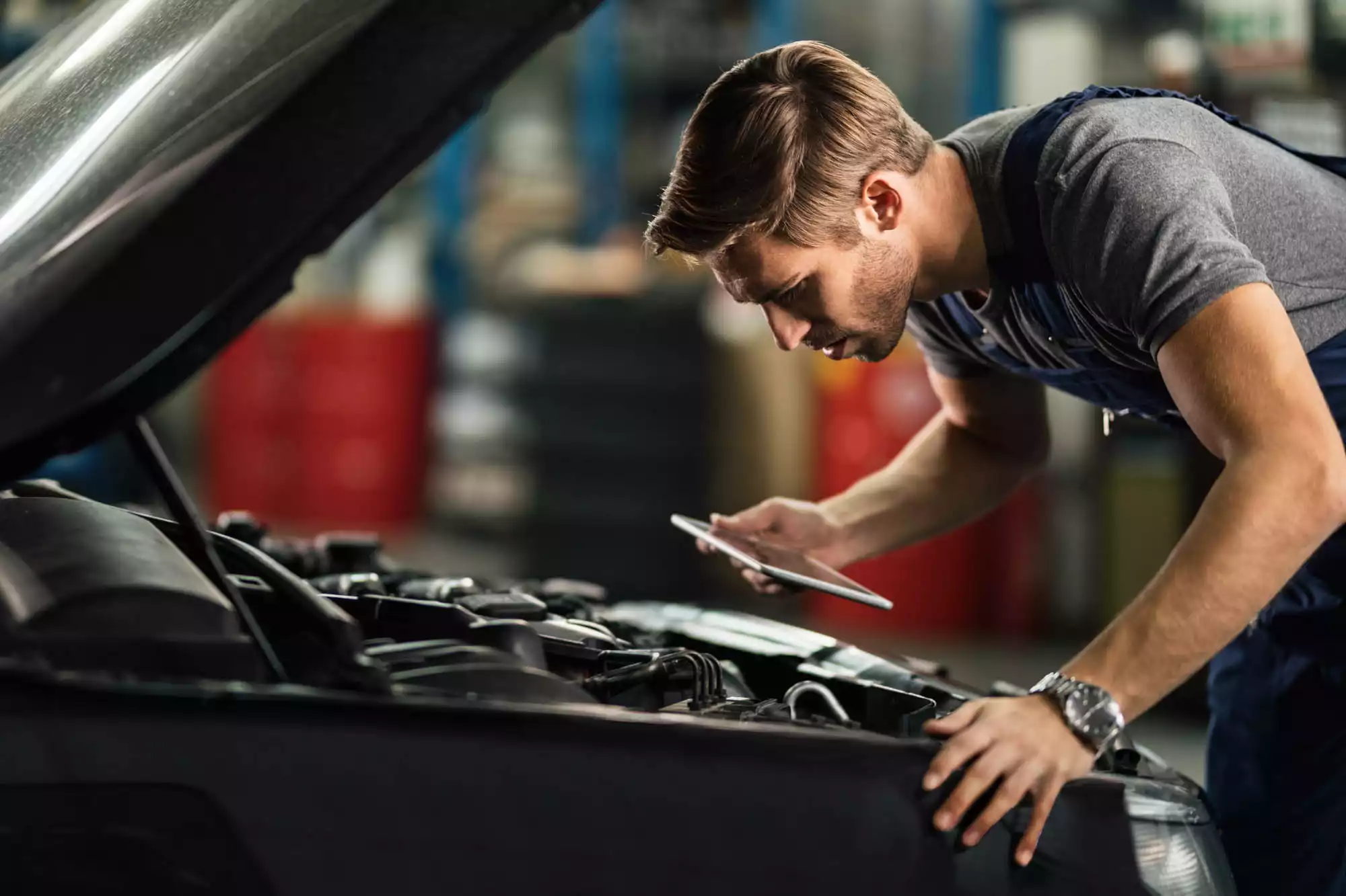 Young,Auto,Mechanic,With,Touchpad,Examining,Car,Engine,In,Repair