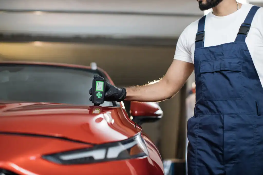 mechanic using tool to check car paint thickness