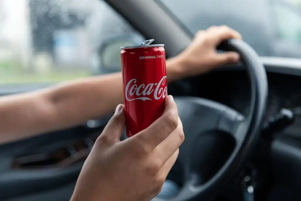 driver holding a coca cola can inside a car