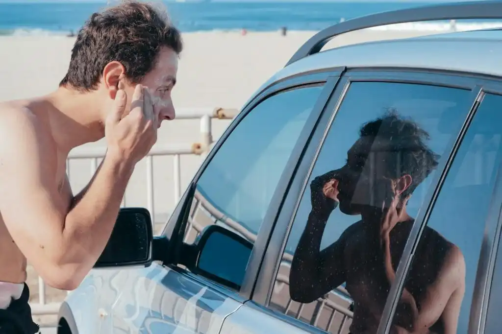 man applying sunscreen beside a car